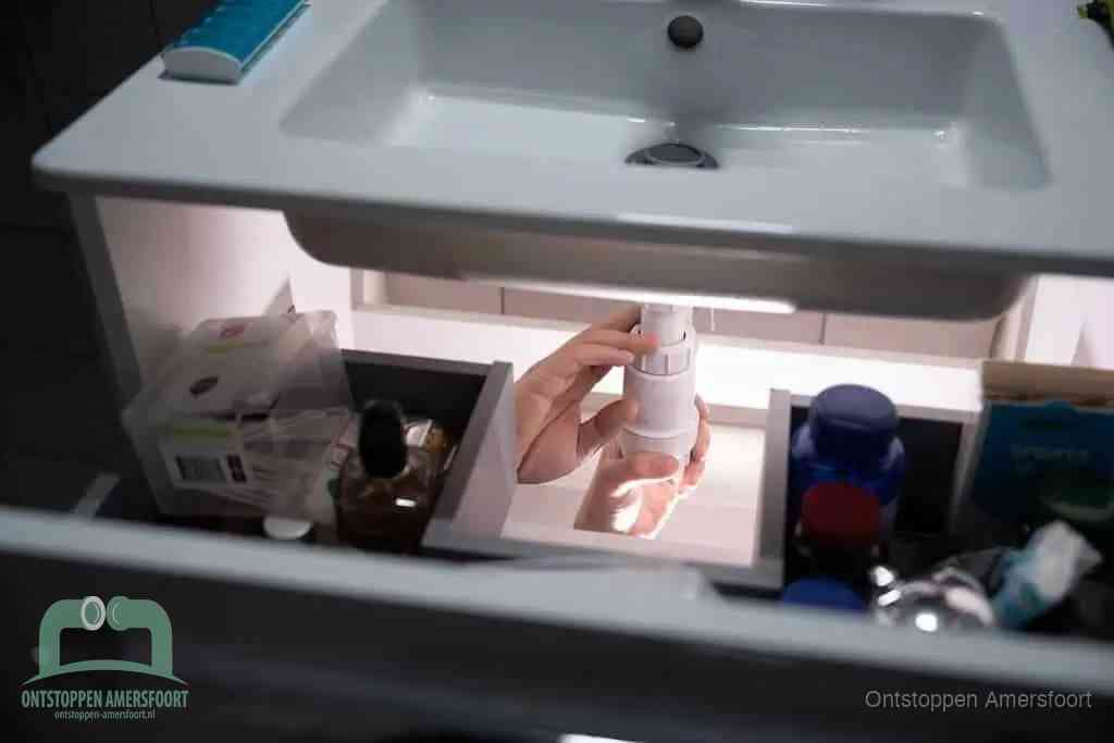 Een pompfles met zeep boven een wastafel, de heet water en afwasmiddel-methode om een vetprop in de afvoer los te maken in Amersfoort