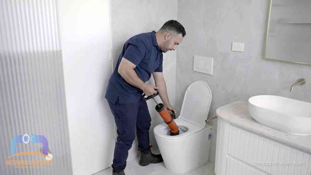 Een monteur buigt over een wandcloset en duwt met de hand een persluchtontstopper in de toiletpot om de verstopping handmatig los te maken in Amersfoort
