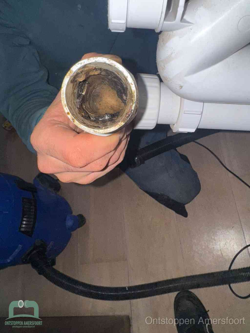 Een hand houdt een losgekoppeld PVC-afvoerbuisstuk vast dat van binnen volledig is dichtgeslibd met vet, vuil en aanslag, de meest voorkomende oorzaak van een verstopte afvoer in Amersfoort