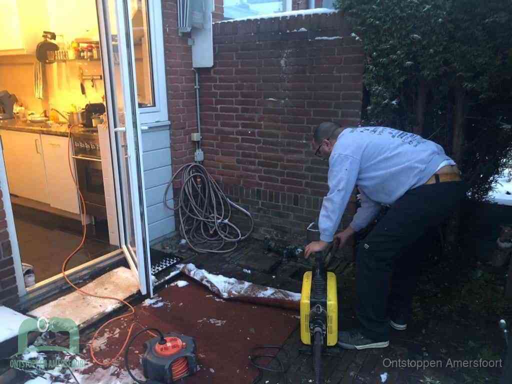 Een monteur werkt buiten bij een open riool-/grondput met een elektrische ontstoppingsmachine om een verborgen afvoerprobleem op te sporen in Amersfoort