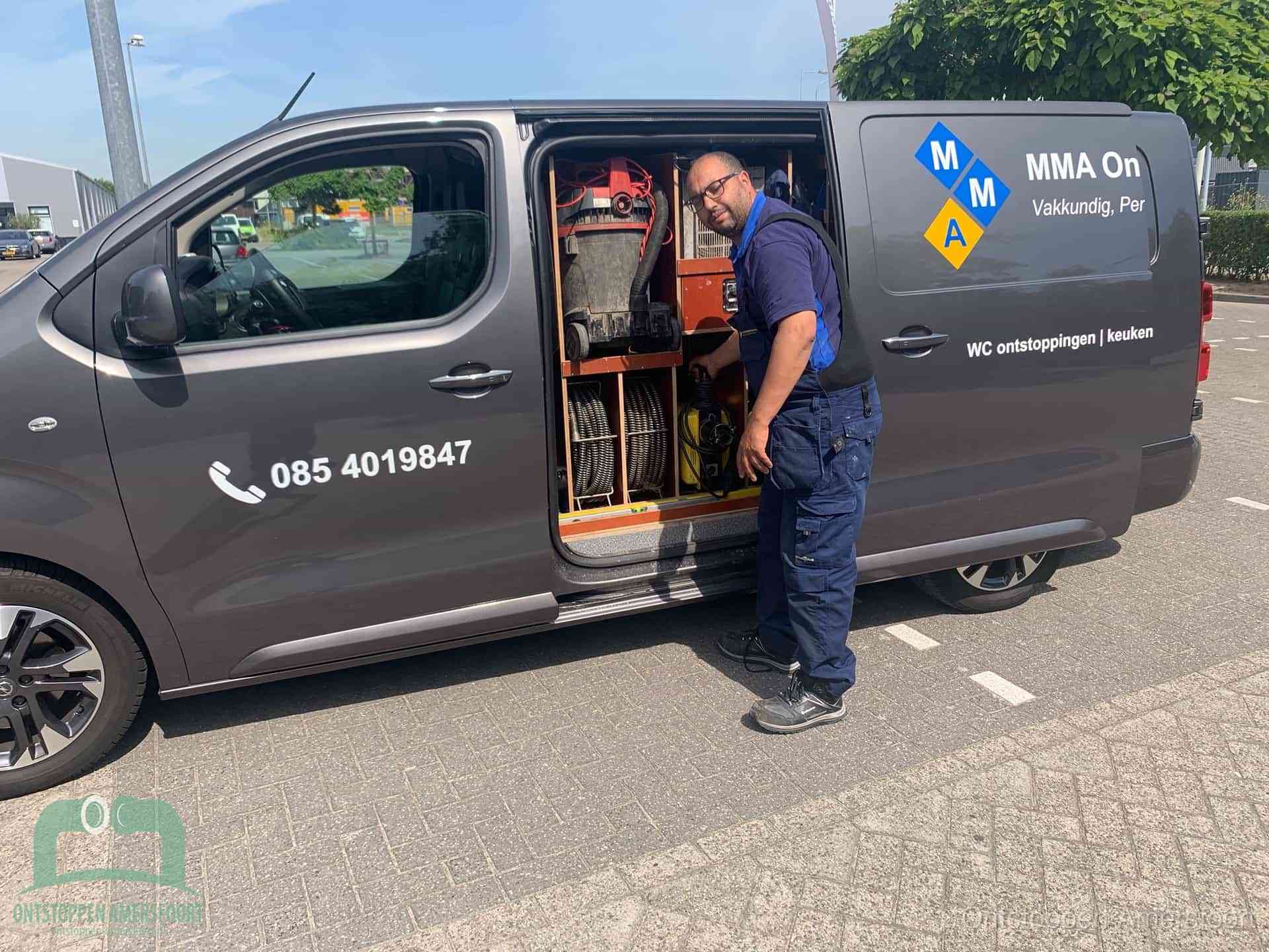 Een monteur bij de open schuifdeur van zijn bedrijfsbus op een parkeerplaats, klaar om de oorzaak van terugkerende afvoerverstoppingen aan te pakken in Amersfoort