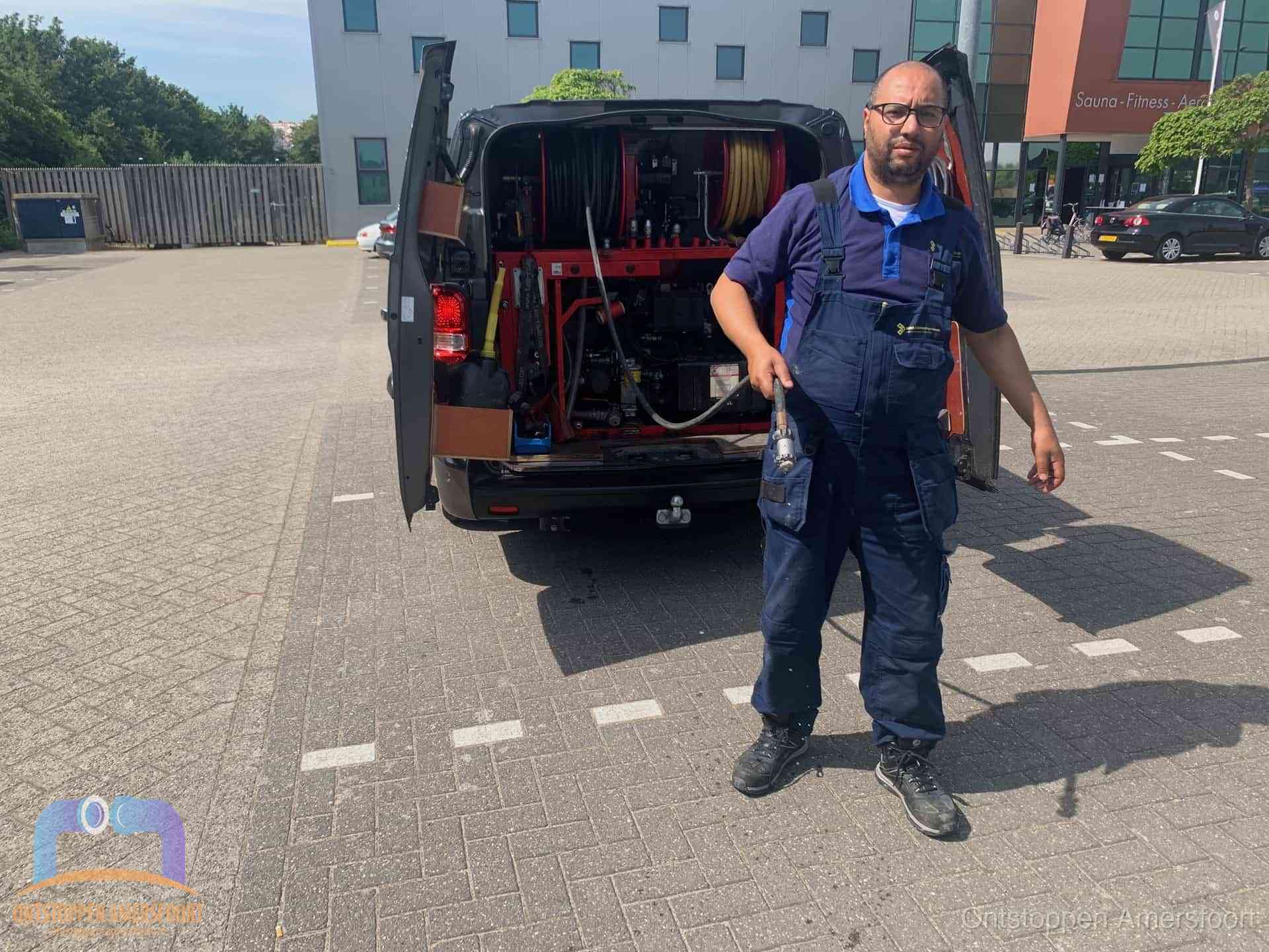 Een monteur bij zijn bestelbus met een hogedruk- en rioolreinigingsunit, klaar om de oorzaak van terugkerende wc-verstoppingen aan te pakken in Amersfoort
