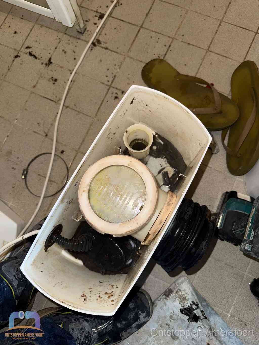 Een gedemonteerde toiletpot op de vloer met ontstoppingsveer en gereedschap ernaast, het verwijderen van een vastzittend voorwerp uit de wc in Amersfoort