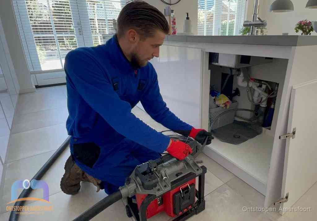Een monteur voert een professionele elektrische ontstoppingsmachine in de afvoer onder de spoelbak tijdens het gootsteen ontstoppen in Amersfoort