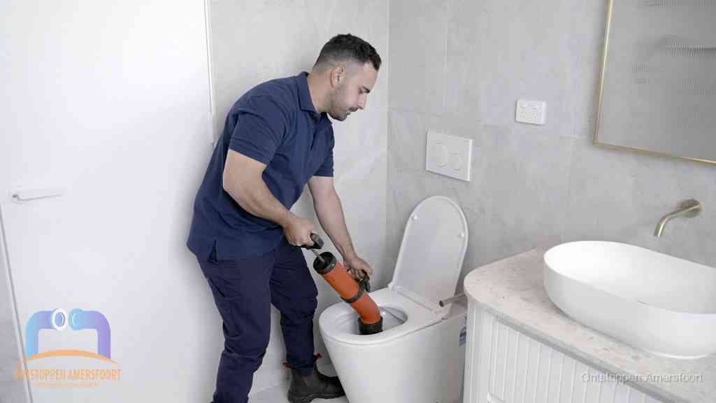 Een monteur gebruikt een handmatige perspomp (toiletontstopper) op een wandcloset tijdens het professioneel wc ontstoppen in Amersfoort