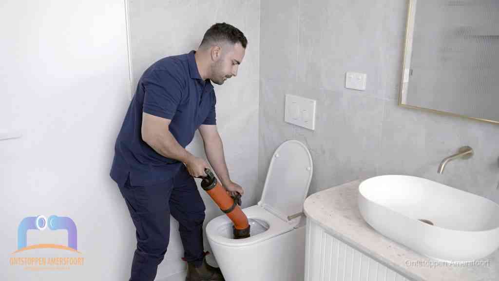 Een man gebruikt een handmatige luchtdruk-ontstopper in een modern betegeld toilet om zelf de wc te ontstoppen in Amersfoort